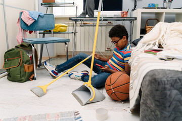 Black boy using cellphone while doing housework at his room © Drobot Dean