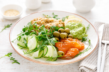 Oatmeal with salted salmon, avocado guacamole and fresh vegetable salad of arugula, cucumbers and olives. Breakfast
