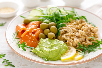 Oatmeal with salted salmon, avocado guacamole and fresh vegetable salad of arugula, cucumbers and olives. Breakfast