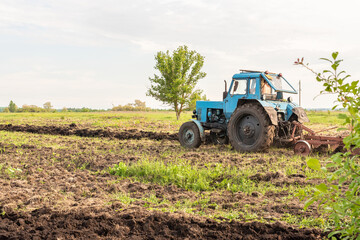 Old blue tractor on the field working. Farmer plowing stubble field in tractor preparing plows the land, agricultural works at farmlands, agriculture tractor-landscape. Tractor Plowing.