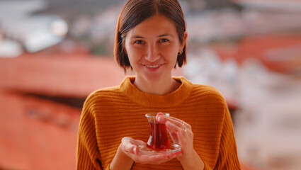 Woman drinking turkish tea from traditional turkish teacup and enjoys panorama over sunset of Kas...