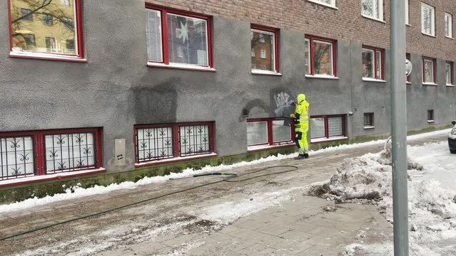 Unrecognizable man removes graffiti from building in winter in Sweden