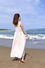 Fototapeta na wymiar 海岸でポーズをとる白いワンピースを着た若い女性の後ろ姿