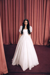 Fototapeta premium Bride in a white wedding dress in the ceremonial hall. Significant day. Burgundy background.