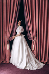 Bride in a white wedding dress in the ceremonial hall. Significant day. Burgundy background.
