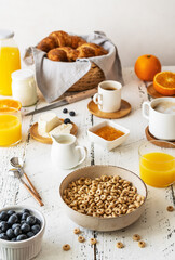 Obraz na płótnie Canvas Breakfast concept with cup of coffee, croissants, wholegrain hoops, milk, orange juice, yogurt and blueberries