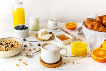 Fototapeta na wymiar Breakfast concept with cup of coffee, croissants, wholegrain hoops, milk, orange juice, yogurt and blueberries