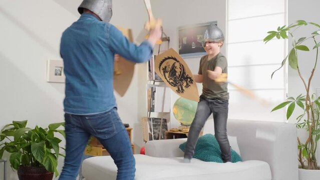 Son and father disguised with helmets sword and shield having fun playing medieval swords fight.   Father is being defeated