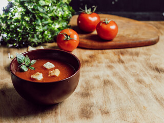 tomato soup in a brown plate stands on a wooden background, rustic