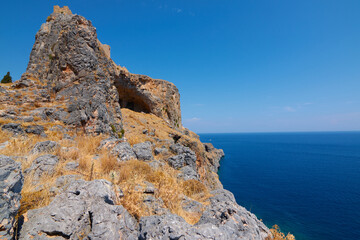 Rocky peak with dry vegetation on the coast against the backdrop of the blue sea