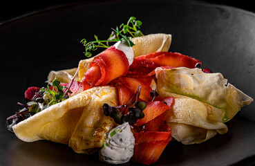 Crepes with smoked gravlax salmon on black plate on wooden table dark background