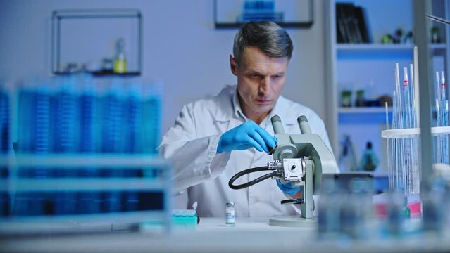 Serious lab scientist studying bacteria under microscope, vaccine development