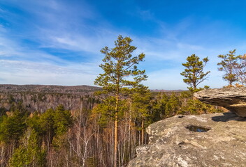 Autumn landscape with trees and rocks on top of a mountain against a background of forest and sky