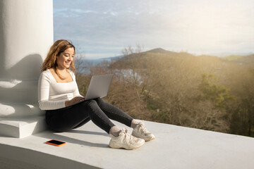 Cheerful woman browsing laptop near column