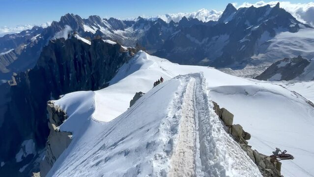 POV camera climber walking narrow path on mountain ridge under Aiguille du Midi 3842m with French Alps mountains peaks panorama. Beauty of Nature and extreme people activity concept