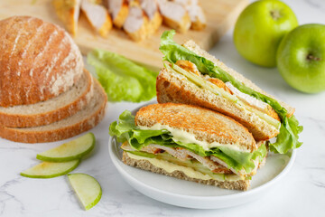 Grilled organic chicken sandwich with green apple, lettuce and cheese sauce on whole grain bread. Delicious and healthy breakfast in a white plate on a marble background. Selective focus - 487605104