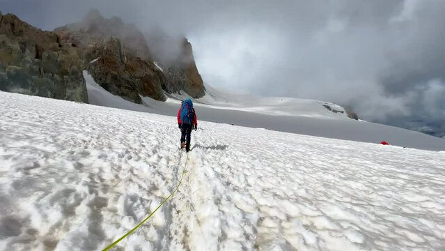 Two persons Rope team crossing the glacier dressed mountaineering clothes walking under Aiguille du Midi 3842m peak. People extreme activities sporty concept 4K handheld video.