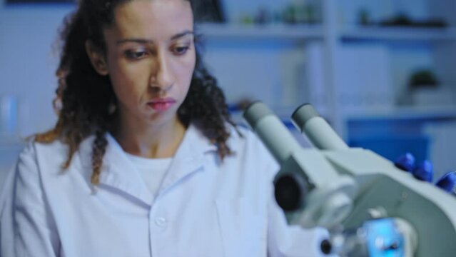 Female lab assistant examining sample under microscope, testing product quality