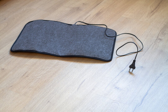 An electric mat for drying wet shoes lies on the floor