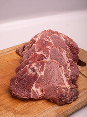 Pork meat cut into chops, slices, on a wooden chopping board, on a white. Raw pork neck steaks, cutlets, close up.
