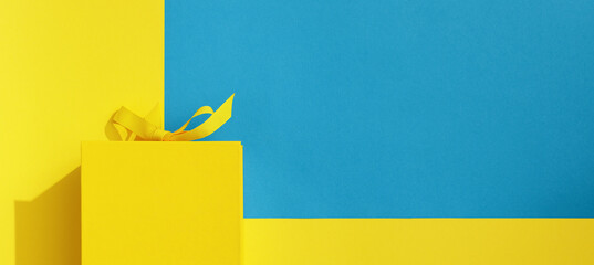 Bright yellow gift box with ribbon bow on yellow and blue  background top view copy space. Birthday present, March 8, Mothers Day, Valentines Day, Easter or spring concept.
