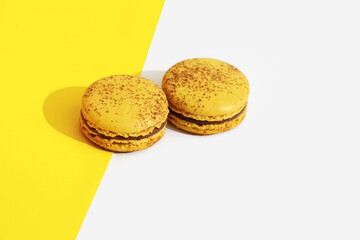 Two Yellow french macaroons on bright yellow and white background.  Delicious meringue cookies. Food concept