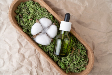 A green dropper bottle of face serum or natural oil lying on a moss