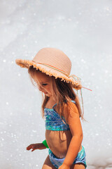 A small child playing contentedly in foam in a straw hat and swimsuit at a foam party in the summer