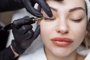 Close-up of a woman, in a beauty salon with her eyes closed, a cosmetologist makes permanent...