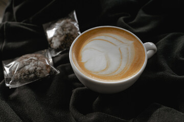 a cup of cappuccino stands on a black cloth, chocolate chip cookies lie nearby