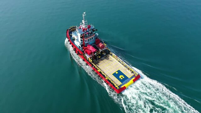 Aerial drone tracking video of assistive tug boat cruising in Mediterranean logistics port