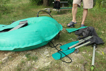 In the morning, a young European pumps an inflatable rubber boat with a foot pump on the bank of a fishing pond. Preparing for the morning fishing on the lake in a boat outdoors in the summer season