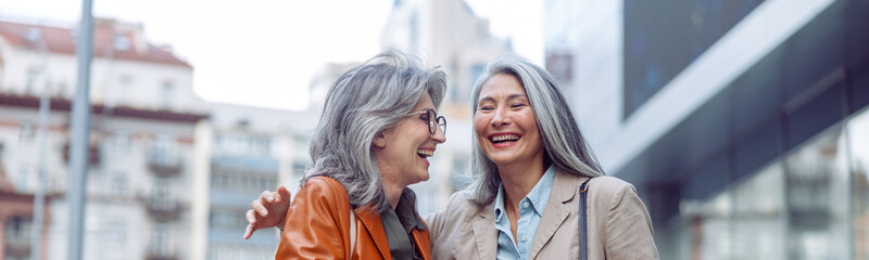 Beautiful grey haired senior women companions on modern city street at walking on nice autumn day. Friends spend time together