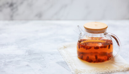 Glass teapot with hot tea with goji berries on a bamboo stand. Selective focus.