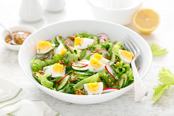 Easter fresh vegetable salad with boiled egg, radish and cucumber, dressing with dijon mustard and lemon on white wooden table