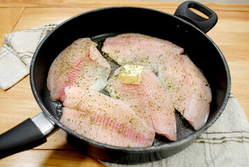 Fresh Tilapia Frying in a Black Pan with Butter and Herbs