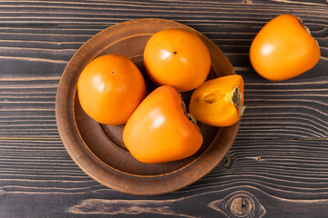 A group of ripe orange persimmon fruits.Persimmon fruits in a plate, rustic background, Persimmon fruits. Selective focus.