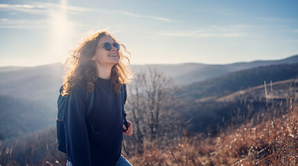 Young woman with a backpack enjoying nature walking on a spring day in the mountains at sunset