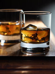 Two glasses of whisky on the rocks on a wooden bartop