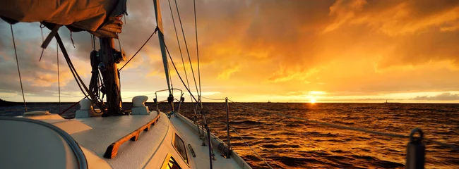 Foto auf Glas White yacht sailing in an open sea at sunset. A view from the deck to the bow, mast, sails. Epic cloudscape. Dramatic sky with glowing golden clouds after the storm. Racing, sport, leisure activity © Aastels