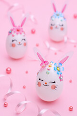 Pink Easter composition. Three white Rabbit Eggs with flowers, ears and muzzles on a pink background decorated with ribbons and beads. Greeting Easter card.