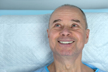 close-up of mature charismatic man, senior 60 years lies in blue hospital gown in clinic, male...