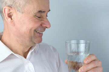 close-up of mature charismatic man, senior 60 years drinks clean water from glass, takes pill, concept most important element for life, human health, quench thirst