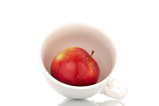 One juicy, ripe, red apple with a white ceramic cup, macro, isolated on a white background.
