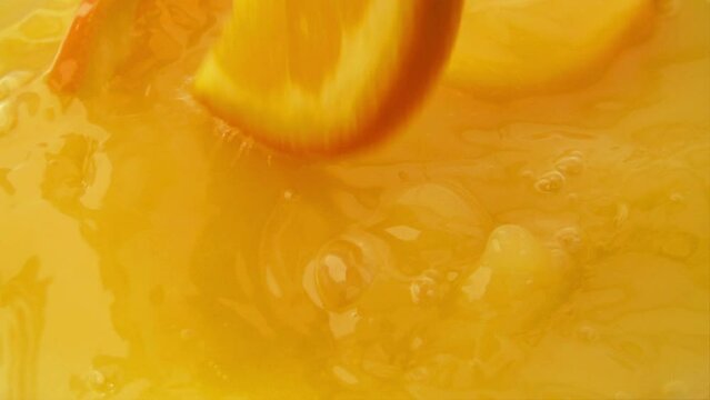 Orange slices falling into juice. Slow motion.