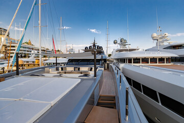 Fototapeta premium The front deck of huge yacht in port of Monaco at sunset, the place for landing of helicopter, a lot of motorboats are on background, the chrome plated handrail, megayacht is moored in marina, dusk