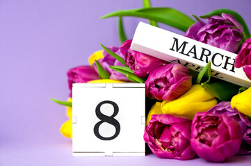 Wooden calendar with 8 march date near a bunch of colorful tulips