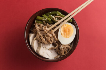 Asian food ramen noodles with meat, vegetables and egg in brown bowl on red background