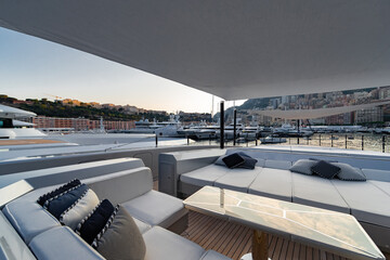 The front deck of huge yacht in port of Monaco at sunset, the place for landing of helicopter, a lot of motorboats are on background, the chrome plated handrail, megayacht is moored in marina, dusk