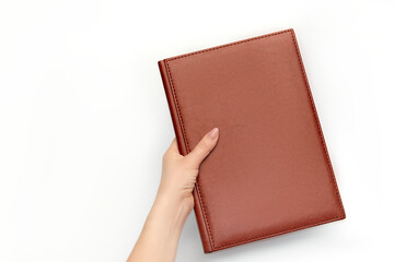 A woman's hand holds an empty brown leather book diary, note cover isolated on white in studio.